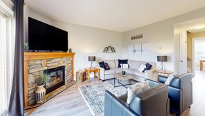 A living room with a stone fireplace, a flat-screen TV, a grey sofa set, and a coffee table. - Bright 3BDR Condo Near Blue | Dog Friendly (The Blue Mountains)