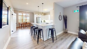 A modern kitchen with a central island, bar stools, and a dining area with chairs. - Bright 3BDR Condo Near Blue | Dog Friendly (The Blue Mountains)