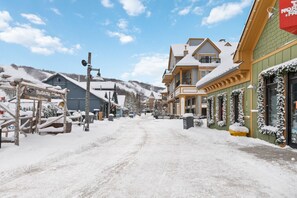 Una calle cubierta de nieve con edificios, incluyendo un centro de calentamiento y un hotel con la entrada nevada.