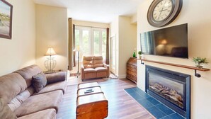 A living room with a sofa, armchair, fireplace, television, and a clock on the wall. - 2BDR Family Getaway - Mountainside & Close to Blue (The Blue Mountains)