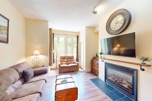 Una sala de estar con sofá, sillón, chimenea, televisión y un reloj en la pared.