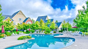 Ein Schwimmbecken mit Liegestühlen und Sonnenschirmen, umgeben von Häusern mit unterschiedlicher Architektur.