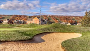 Un campo da golf con una bunker di sabbia, case sullo sfondo e cielo sereno.