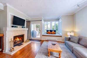 A living room with a fireplace, a television, a sofa, and a window seat with cushions. - Slopeside Retreat w/ Wood Fireplace & Mins to Blue (The Blue Mountains)