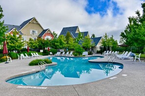 Ein Swimmingpool mit Liegestühlen, einem flachen Bereich und Häusern im Hintergrund.