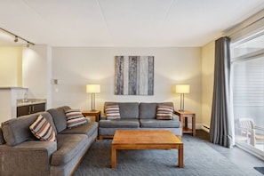 A modern living room with a sofa set, a coffee table, two side tables with lamps, a painting on the wall, and a view through a large window. - Ground-Floor Steps to Blue Mountain Home for 4 (The Blue Mountains)