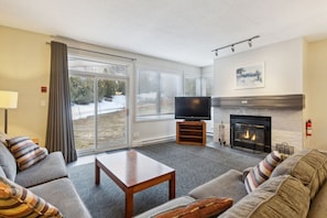 A living room with a sofa, a coffee table, a flat-screen TV, a fireplace, and large windows. - Ground-Floor Steps to Blue Mountain Home for 4 (The Blue Mountains)