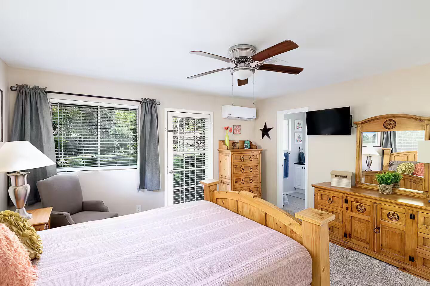 A bedroom with a bed, a ceiling fan, a dresser, a TV, and a window with curtains.