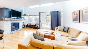 Amplia sala de estar con chimenea, asientos cómodos, televisor de pantalla plana y ventanas grandes.