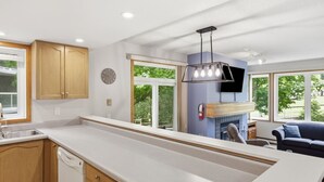 A modern kitchen with wooden cabinets, a dishwasher, a built-in oven, and a large window overlooking a garden. - 3 Bedroom Home | Steps to Blue Mtn Village (The Blue Mountains)