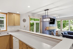 Una cocina moderna con armarios de madera, lavavajillas, horno integrado y un amplio ventanal con vistas a un jardín.