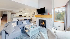 Ein modernes Wohnzimmer mit Kamin, Fernseher und Blick ins Freie.