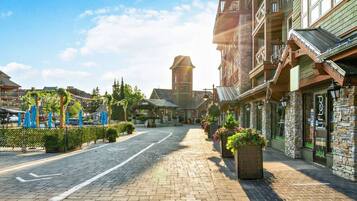 A cobblestone street lined with stone buildings, a church tower, and outdoor seating areas with umbrellas.