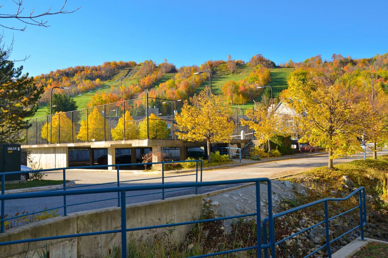 A parking structure with a concrete roof and metal railings, surrounded by autumn foliage and a clear blue sky.