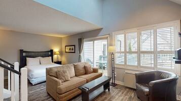A hotel room with a bed, a sofa, a chair, a small table, and a window with blinds.