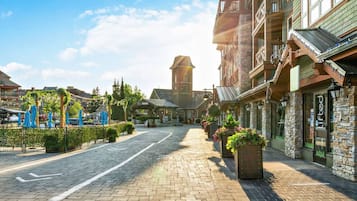 A cobblestone street lined with stone buildings, a church tower, and outdoor seating areas with umbrellas.
