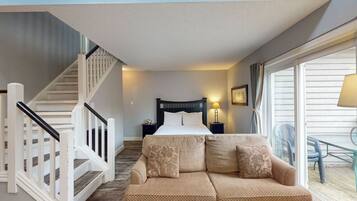 A bedroom with a bed, a sofa, a staircase, a nightstand, and a window.