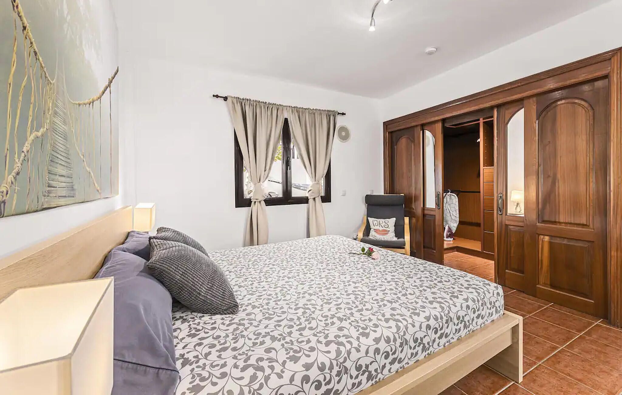 A bedroom with a bed, a chair, a wardrobe, and a painting on the wall.