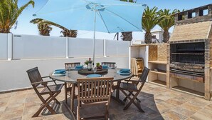 A round glass table with wooden chairs, a blue umbrella, and a stone barbecue grill. - Stunning home in Tahiche with private swimming pool, can be inside or outside (Tahiche)