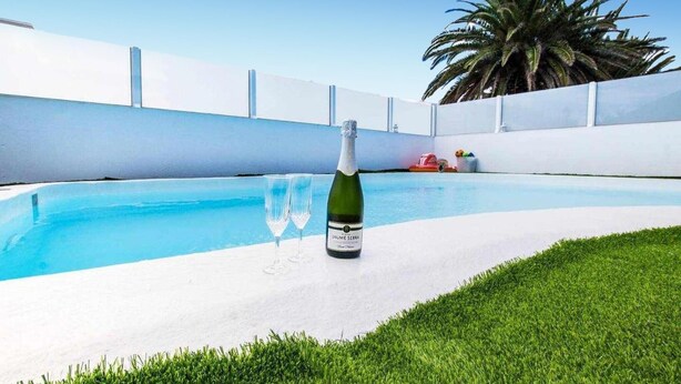 A pool with a bottle of champagne and glasses on the edge, surrounded by a white wall and a palm tree. - Stunning home in Tahiche with private swimming pool, can be inside or outside (Tahiche)