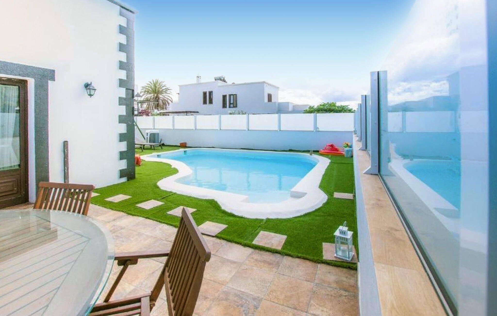 Un jardin avec une piscine, une table en verre et une chaise.