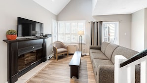 Ein Wohnzimmer mit Kamin, Fernseher, Sofa und einem Fenster mit Jalousien.