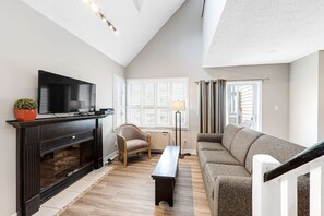 A living room with a fireplace, television, sofa, and a window with blinds. - North Creek Nest at BM with Pool, Hot Tub, Tennis (The Blue Mountains)