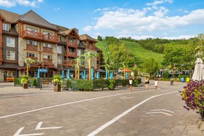 A hotel with a stone facade, multiple balconies, and a paved courtyard with umbrellas. - North Creek Nest at BM with Pool, Hot Tub, Tennis (The Blue Mountains)