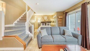 A living room with a grey sofa, wooden coffee table, and a staircase. - Family North Creek Condo w/ Pool, Hot Tub, Tennis! (The Blue Mountains)