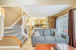 Ein Wohnzimmer mit grauem Sofa, Holztisch und einer Treppe.