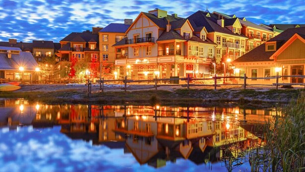 A waterfront hotel with multiple buildings, a reflective lake, and a dock with kayaks. - Family North Creek Condo w/ Pool, Hot Tub, Tennis! (The Blue Mountains)