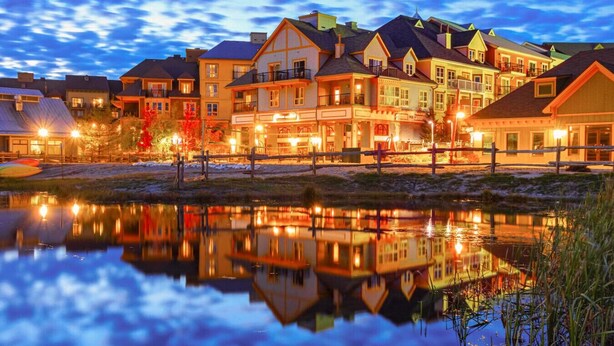 Un hôtel situé au bord d’un lac, composé de plusieurs bâtiments, dont le reflet se mire dans l’eau, et doté d’un quai avec des kayaks.
