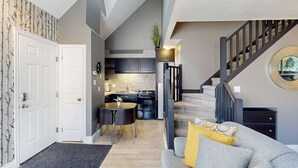 A modern kitchen with dark cabinets, a dining area with a round table and chairs, and a staircase with a decorative railing. - The Adventure Pad: Pool, Hot Tub, Tennis! (The Blue Mountains)