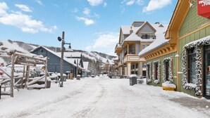 Una calle nevada con edificios, incluyendo un letrero de centro de calentamiento, y un hotel con un anuncio de una tienda cercana.