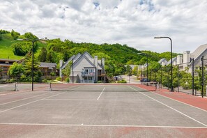 An outdoor tennis court with a net, surrounded by buildings and greenery. - Cozy Creek Retreat: Pool, Hot Tub, Tennis! (The Blue Mountains)