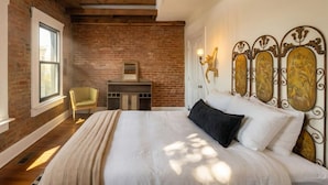 Une chambre avec un mur en briques, un lit avec une literie blanche, une tête de lit en bois et un petit bureau avec une chaise.