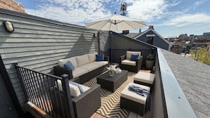 Une terrasse sur le toit, aménagée avec du mobilier d’extérieur, une rambarde et offrant une vue sur le paysage urbain.