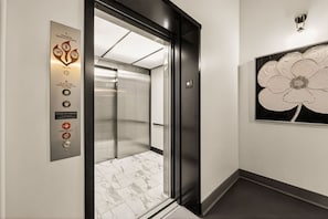 An elevator with a control panel, a marble floor, and a large floral artwork on the wall. - Luxury 3BR on TQL Stadium & Washington Park (Cincinnati)
