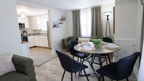 Een moderne woonkamer met een eettafel, zwarte stoelen, een bank en een keuken op de achtergrond.
