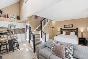 Ein kompakter Wohnraum mit Küchenzeile, Treppe, Bett und Schlafsofa.