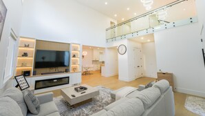 Ett modernt vardagsrum med en platt-TV, en soffa, ett soffbord och en matplats med ett glasräcke.