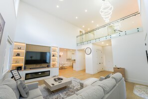 A modern living room with a flat-screen TV, a sofa, a coffee table, and a dining area with a glass railing. - Luxury Okanagan House in heart of Kelowna! (Kelowna)