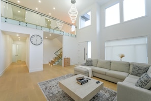 A spacious living area with a high ceiling, a staircase, a sofa set, and a coffee table with books. - Luxury Okanagan House in heart of Kelowna! (Kelowna)