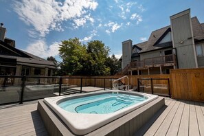 Un bain à remous sur une terrasse en bois, avec vue sur les bâtiments et les arbres.