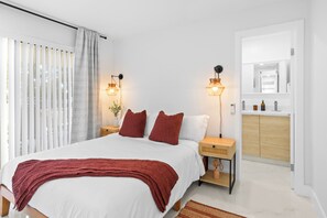 A modern bedroom with a large bed, bedside lamps, a wooden nightstand, a mirror, and a built-in wardrobe. - Beautiful 3-bedroom house with AC in Fort Lauderdale near Beach,Downtown,Airport (Fort Lauderdale)