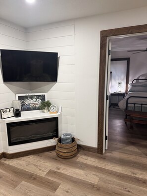 Uma sala de estar moderna com televisão de tela plana sobre a lareira, uma mesinha com objetos decorativos e um cesto de vime no chão.