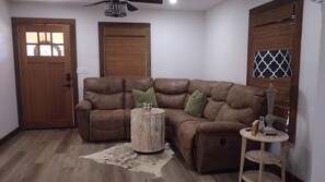 Ein Wohnzimmer mit einem braunen Ledersofa, einem runden Holztisch und einem Beistelltisch mit Lampe.