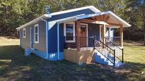 A small, single-story house with a porch and a staircase leading to the entrance. - Happy Acre of Wolfpen a charming little 2 bed 1 bath home (Mena)