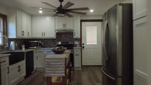 A modern kitchen with white cabinets, a stainless steel refrigerator, a microwave, and a ceiling fan. - Happy Acre of Wolfpen a charming little 2 bed 1 bath home (Mena)
