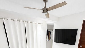 Een slaapkamer met een bed, een plafondventilator, een aan de muur bevestigde televisie en een deur.